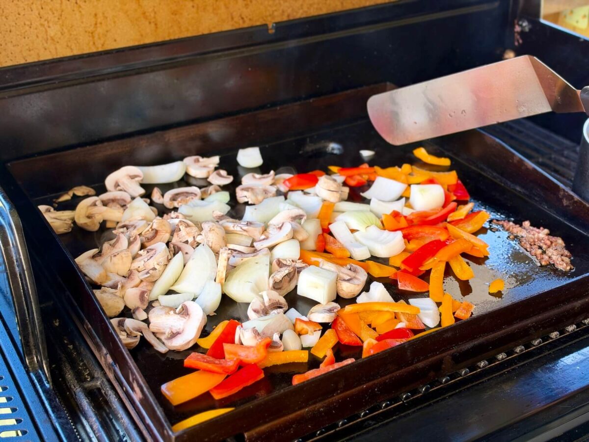 sautéing chopped bell peppers, onions, and mushrooms on a griddle