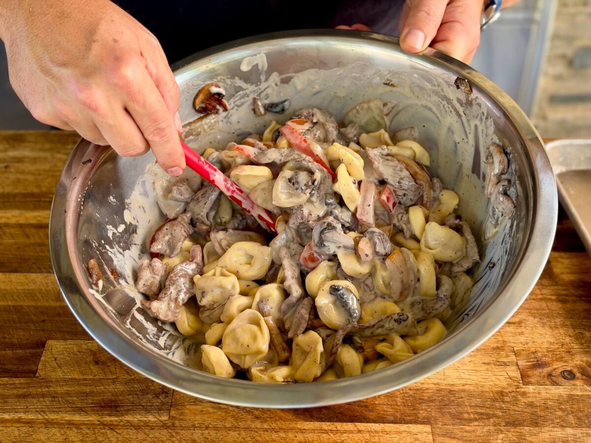 mixing cheese sauce, cooked sliced ribeye steak, tortellini pasta, and sautéed peppers and onions in a large mixing bowl