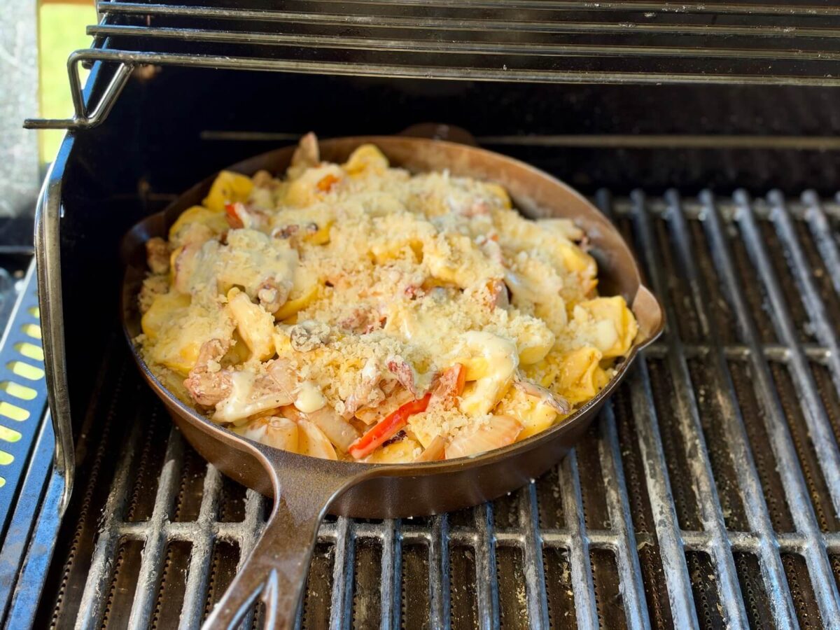 cooking cheesesteak tortellini in a cast iron skillet on a grill