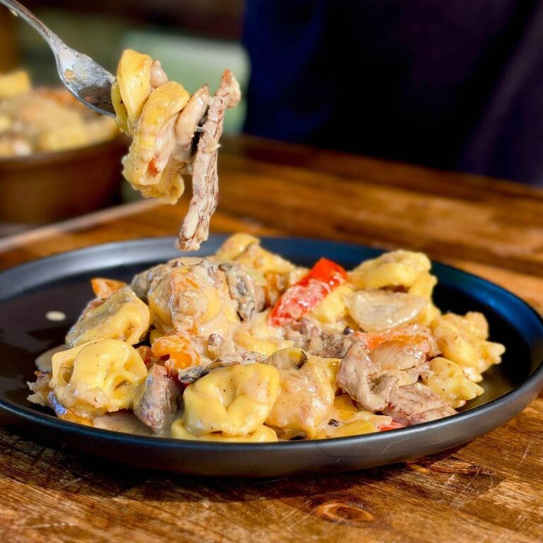 Philly cheesesteak tortellini with sliced ribeye steak, cheese tortellini, bell peppers, and onions on a plate